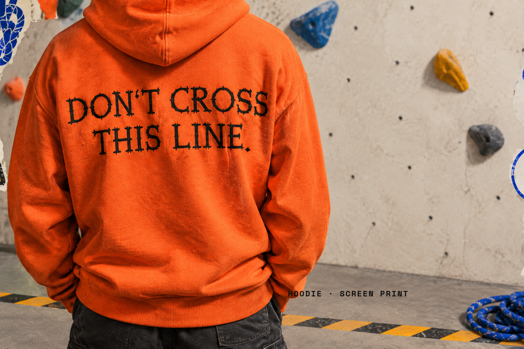 Orange hoodie with DON'T CROSS THIS LINE printed in Belay Knot, worn at a climbing wall